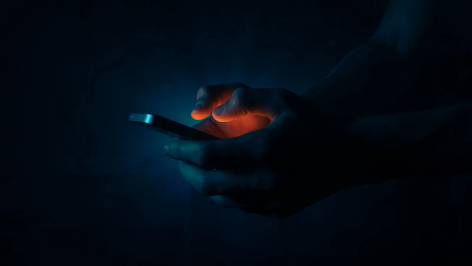 Hände halten ein Handy im Dunkeln, das Licht des Bildschirms fällt auf die Finger