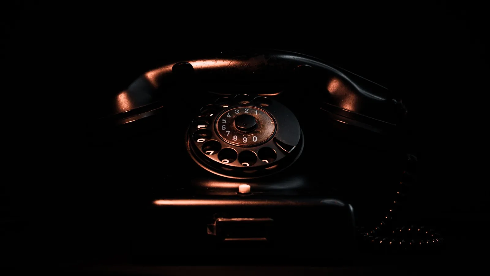Altes schwarzes Wählscheibentelefon im Dunkeln, seitlich warm angeleuchtet