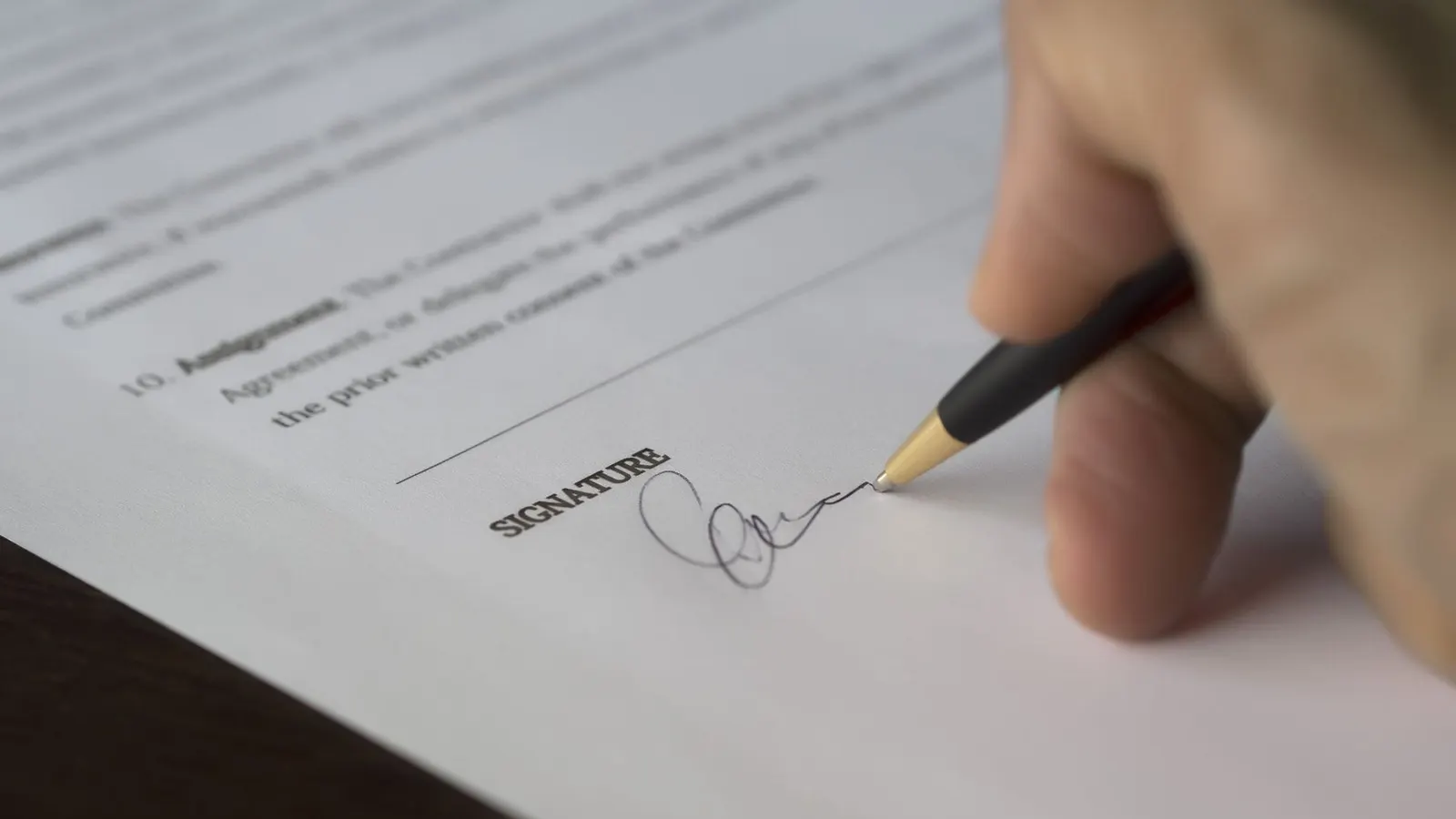 Eine Hand unterschreibt einen Vertrag mit einem Stift
