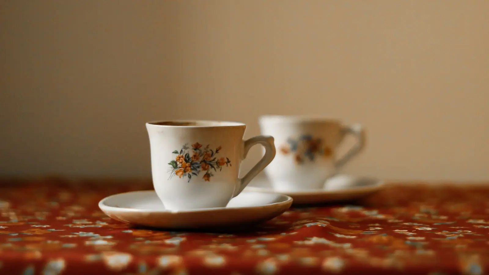 Zwei Kaffeetassen mit Blumenmuster vor einer hellen Wand